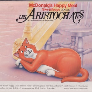 Puede incluir: Un Happy Meal de McDonald's con la película clásica de Disney "Los Aristogatos". La imagen muestra un gato naranja de dibujos animados acostado en un suelo de baldosas. El texto en la caja dice "McDonald's Happy Meal Walt Disney's Classic Les Aristocats Actuellement dans les salles."