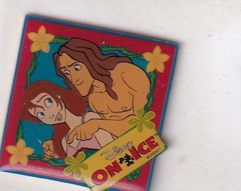 Può includere: Uno spillo da disegno animato rosso, blu e verde con un uomo e una donna con il testo "Disney On Ice" in giallo e nero.