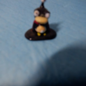 May include: A small black and yellow penguin figurine with a red scarf. The penguin is standing on a black base.