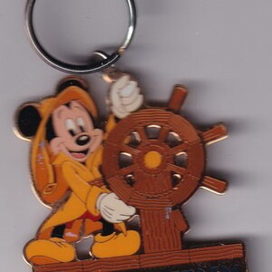 May include: A gold-colored metal keychain featuring Mickey Mouse dressed as a sailor, holding a ship's wheel. The keychain has the text "Ahoy! Cast Aweigh!" on the bottom.