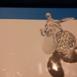 Puede incluir: Una figurita de cristal de Dumbo el elefante de la pel&iacute;cula animada de Disney. La figurita es transparente con ojos azules y un sombrero blanco.