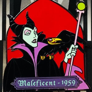 Op de afbeelding: Een zwarte en paarse emaille pin met Maleficent uit de Disney-film Doornroosje. Ze is afgebeeld met haar kenmerkende hoorns, groene huid en paarse jurk. Ze houdt een staf vast met een groene bol erop en een zwarte raaf zit op haar arm. De pin heeft een paarse banner onderaan met de tekst "Maleficent - 1959".