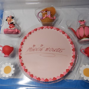 Könnte beinhalten: Ein rosa und rotes Teeset mit einem herzförmigen Teller, auf dem "Minnie Mouse" in schwarzer Kursivschrift steht. Das Set enthält eine Teekanne, zwei Teetassen, eine Untertasse und eine Figur von Minnie Mouse.