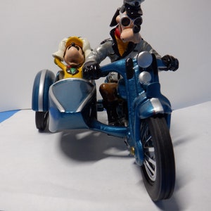 Puede incluir: Una motocicleta azul y plateada con sidecar. La motocicleta tiene un asiento negro y un manillar negro. El sidecar es azul y tiene una figura amarilla sentada dentro.