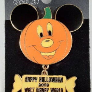 May include: A gold-colored Mickey Mouse Halloween pin featuring Mickey Mouse's head as a pumpkin with a candy cane hanging from the bottom. The candy cane has a yellow banner that reads "Happy Halloween 2002 Walt Disney World" and "Limited Edition".