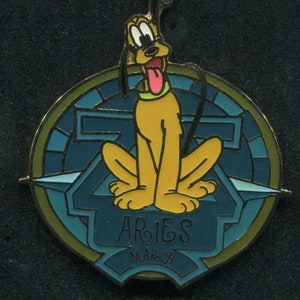 May include: A gold-colored pin with a blue and green background. The pin features a cartoon image of Pluto, the Disney dog, sitting on a blue and green background. The pin also features the text "Aries" and "March".