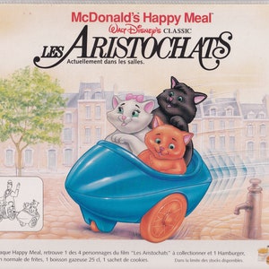 Puede incluir: Un Happy Meal de McDonald's con el clásico de Disney "Los Aristogatos". La imagen muestra tres gatitos montando en un coche de juguete azul. Los gatitos son Marie, Berlioz y Toulouse. El texto "McDonald's Happy Meal" y "Los Aristogatos" es visible en la imagen.