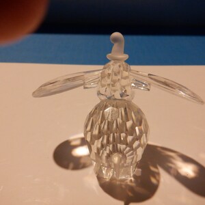 Puede incluir: Una figurita de ping&uuml;ino de cristal transparente que lleva un sombrero blanco. La figurita est&aacute; detallada con muchas facetas y tiene un cuerpo redondeado.