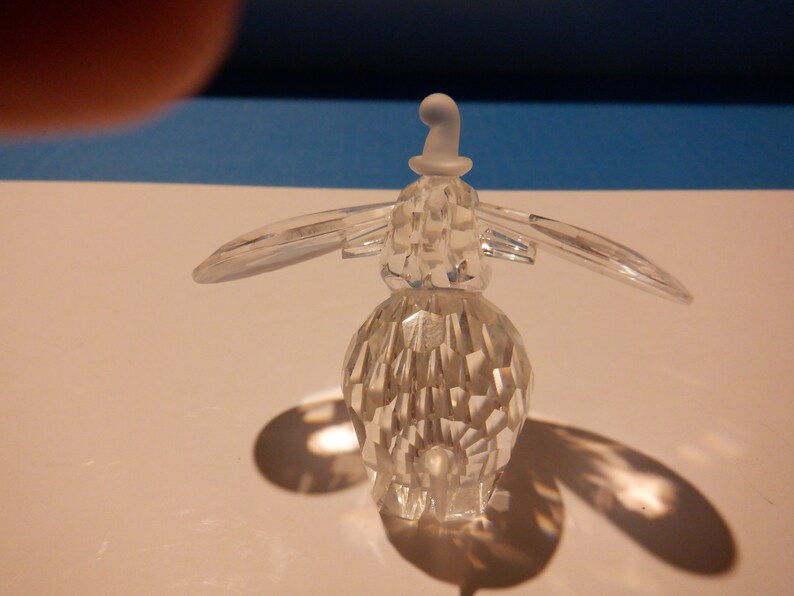 Puede incluir: Una figurita de ping&uuml;ino de cristal transparente que lleva un sombrero blanco. La figurita est&aacute; detallada con muchas facetas y tiene un cuerpo redondeado.