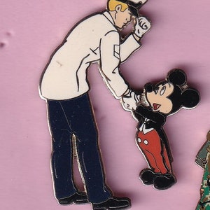 May include: A white and blue cartoon pin featuring Mickey Mouse in a tuxedo, saluting a cartoon sailor in a white uniform and a blue cap.