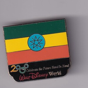 Może przedstawiać: Metalowa odznaka z flagą Etiopii i tekstem "Celebrate the Future Hand in Hand 2000 Walt Disney World" pod flagą.