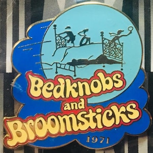 Może przedstawiać: Emaliowana przypinka w kolorze niebieskim i żółtym z tytułem "Bedknobs and Broomsticks" i rokiem 1971 poniżej. Przypinka przedstawia sylwetkę łóżka z trzema postaciami na nim.