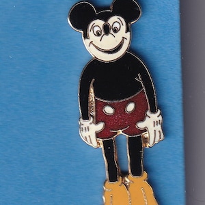 Könnte beinhalten: Eine Mickey Mouse-Anstecknadel in Schwarzweiß mit einer roten und weißen Polka-Dot-Shorts. Die Anstecknadel befindet sich auf einem blauen Hintergrund.
