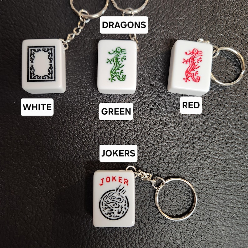 Puede incluir: Cuatro fichas de mahjong de cer&aacute;mica blanca con llaveros. Las fichas presentan un dise&ntilde;o de drag&oacute;n en verde, rojo y negro. Las fichas est&aacute;n etiquetadas como "DRAGON" y "JOKER".