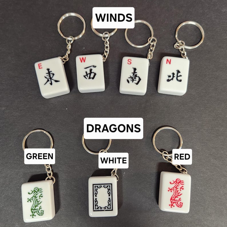 May include: Four white mahjong tile keychains with black characters and red lettering. The tiles represent the four winds: East, West, South, and North. Three white mahjong tile keychains with black and green, black and white, and black and red dragons. The tiles are labeled "Green", "White", and "Red".