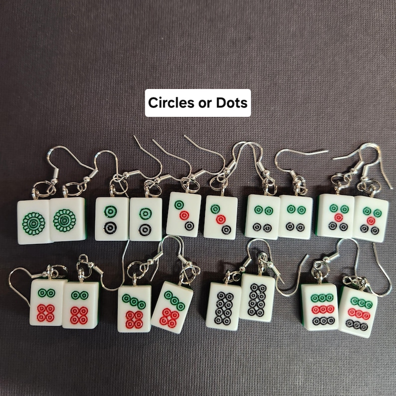 May include: A set of 12 pairs of earrings featuring mahjong tiles with different circle and dot patterns. The earrings are silver with white, green, red, and black details.  Circles or Dots.