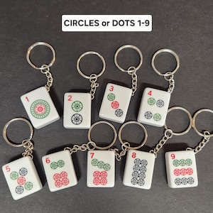 May include: Nine white keychains with silver rings. Each keychain features a white tile with black and green circles and a red number from 1 to 9. The tiles are labeled "CIRCLES or DOTS 1-9".