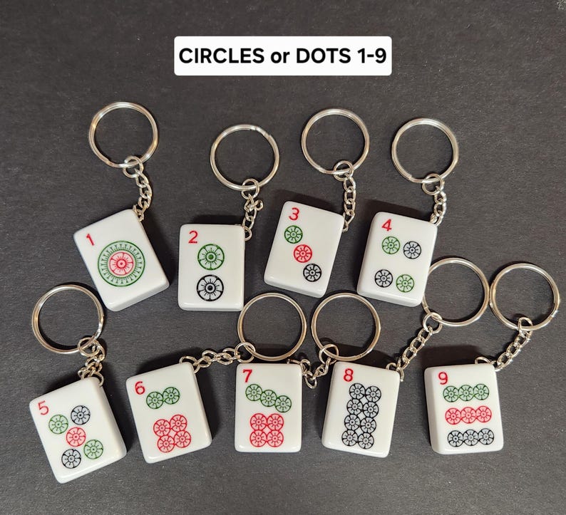 May include: Nine white keychains with silver rings. Each keychain features a white tile with black and green circles and a red number from 1 to 9. The tiles are labeled "CIRCLES or DOTS 1-9".