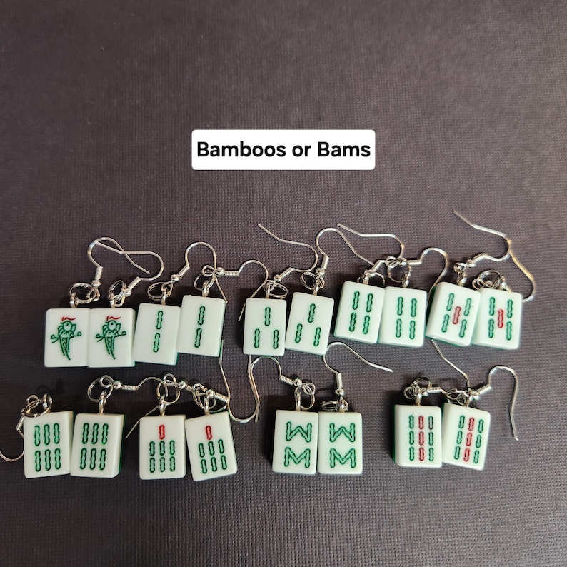 May include: A set of 10 pairs of earrings featuring miniature mahjong tiles. The tiles are white with green and red markings. The tiles depict the numbers 1 through 9 and the wind symbols. The earrings are labeled "Bamboos or Bams".