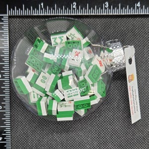 May include: A clear glass Christmas bauble filled with miniature green and white Mahjong tiles. The bauble has a silver cap and a small tag attached. The tiles are scattered inside the glass sphere.