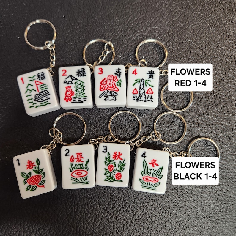 Puede incluir: Ocho llaveros de fichas de mahjong blancas con caracteres y s&iacute;mbolos chinos rojos y verdes. Las fichas est&aacute;n numeradas del 1 al 4 y est&aacute;n etiquetadas como "FLOWERS RED 1-4" y "FLOWERS BLACK 1-4".
