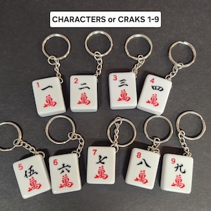 May include: Nine white mahjong tile keychains with black and red characters. Each tile features a number from 1 to 9 and the Chinese character for 'ten thousand'.