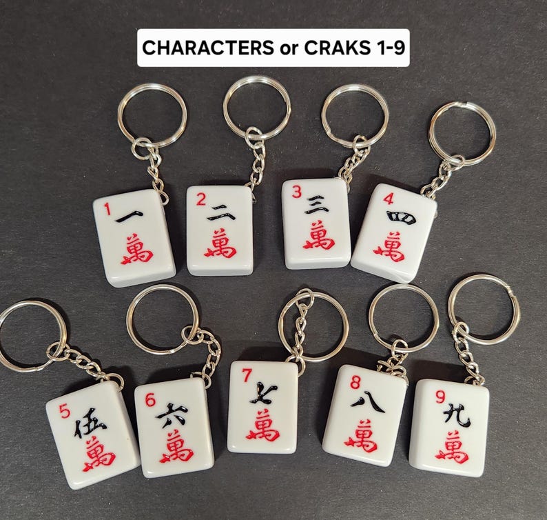 May include: Nine white mahjong tile keychains with black and red characters. Each tile features a number from 1 to 9 and the Chinese character for 'ten thousand'.