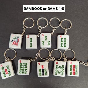 May include: Nine white ceramic keychains with black and green markings, each representing a different number from 1 to 9. The keychains are labeled "BAMBOOS or BAMS 1-9".