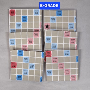 May include: Several Scrabble game boards with a grid design, displaying squares marked "Double Letter Score," "Triple Letter Score," and "Double Word Score." The boards have a neutral colour scheme with red, blue, and pink accents. The text "B-GRADE" is visible.