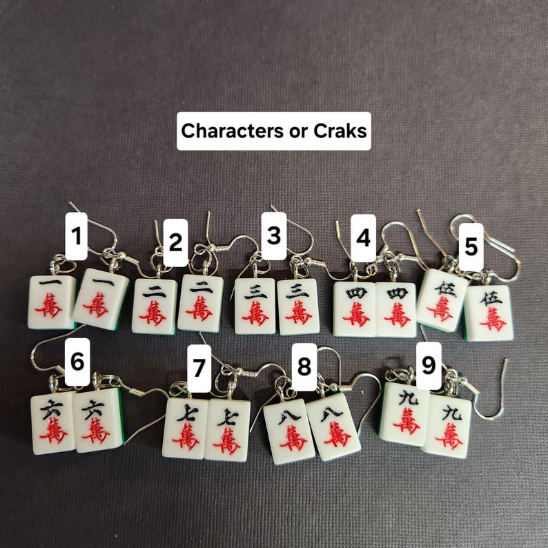 May include: Nine pairs of earrings featuring miniature mahjong tiles with Chinese characters and numbers. The tiles are white with green and red accents. The earrings are silver.