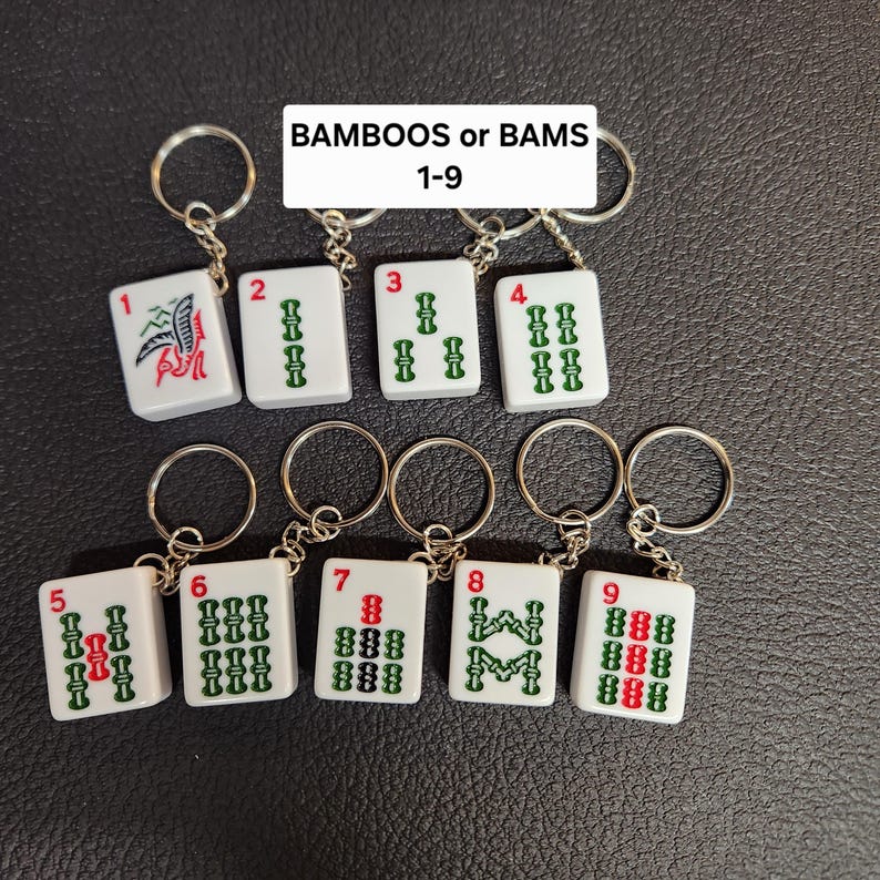 Puede incluir: Nueve fichas de mahjong blancas y verdes con n&uacute;meros rojos en llaveros. Las fichas est&aacute;n numeradas del 1 al 9 y representan el palo de bamb&uacute;. El texto "BAMBOOS or BAMS 1-9" est&aacute; impreso sobre las fichas.