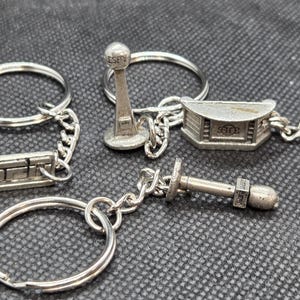May include: A collection of silver-colored keychains. One keychain features the ESPN logo, while others depict a broadcast tower, a news desk, and a bolt. Each keychain has a metal ring and chain.