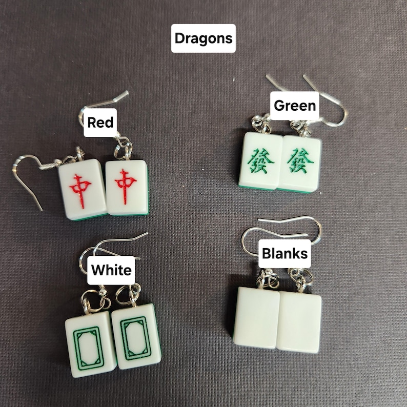 May include: Four pairs of earrings featuring mahjong tiles. The tiles are white with green and red accents. The tiles are labeled "Dragons", "Green", "Red", and "White".