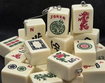 May include: A collection of ivory-colored Mahjong tiles with various symbols and characters in red, green, and black. Some tiles have metal loops attached. The tiles feature images of dragons, flowers, and the word "JOKER".