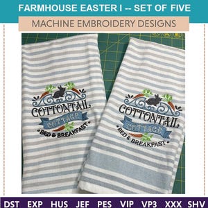 Könnte beinhalten: Zwei weiße Geschirrtücher mit blauen Streifen und gestickten Designs. Das Design zeigt ein schwarzes Kaninchen, Karotten und den Text "Cottontail Cottage Bed & Breakfast".