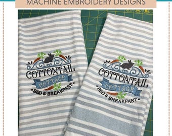 May include: Two white tea towels with blue stripes and embroidered designs. The design features a black bunny rabbit, carrots, and the text "Cottontail Cottage Bed & Breakfast".