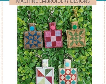 May include: Five machine embroidery designs for quilt block key fobs. The designs feature a variety of colorful quilt blocks, including a star, a checkerboard, a pinwheel, and a diamond pattern. The key fobs are made of brown leather and have silver key rings.