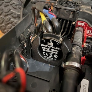 May include: Close-up of a black electric motor with a Spektrum label. The label reads "FIRMA 3200Kv SPMXSM2000." The motor is connected to a red and black wire.