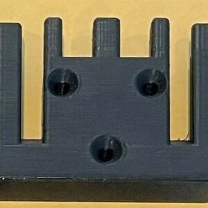 May include: A black plastic 3D printed object with five vertical slots and three circular holes.