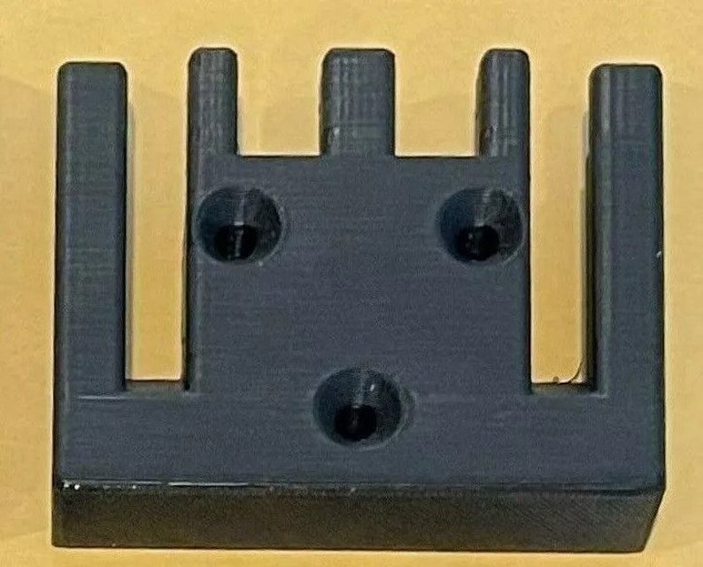 May include: A black plastic 3D printed object with five vertical slots and three circular holes.