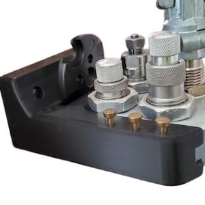 May include: A close-up of a black metal tool with several silver metal attachments. The tool has a rectangular base and a raised section with several small holes. The attachments are cylindrical and have a threaded design.