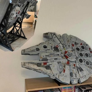 May include: A detailed model of the Millennium Falcon spaceship made from interlocking plastic bricks. The model is primarily gray with red and black accents. It is mounted on a black stand, showcasing the iconic design.