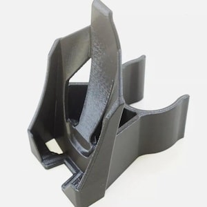 May include: A black 3D printed phone stand with a curved design. The stand is designed to hold a phone upright.