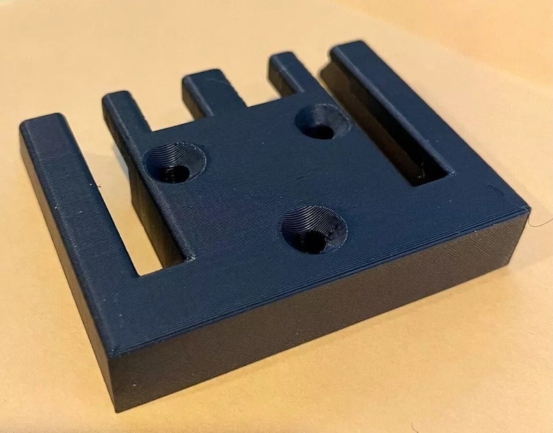 May include: A black plastic 3D printed wall mount with four slots and three screw holes.