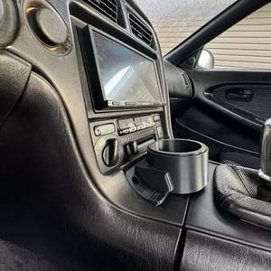 May include: A black car interior with a black cup holder and a black and silver radio.
