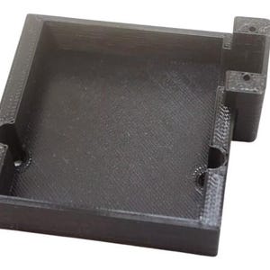 May include: A black plastic box with a square opening and a small rectangular extension on the side. The box has a textured surface and appears to be 3D printed.