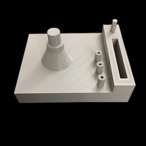 May include: A light gray 3D-printed object with a rectangular base. It features a conical shape, a cylindrical post, three small cylinders, and a rectangular slot. The object is set against a black background.