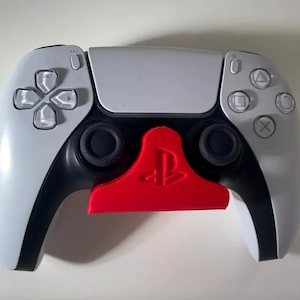 May include: A white and black PlayStation 5 controller with a red PlayStation logo on a wall mount.