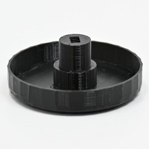 May include: A black plastic cap with a raised center section. The cap has a textured surface and a smooth, round edge.
