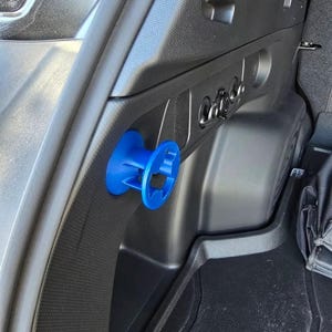 May include: A blue plastic car trunk organizer with a circular design. The organizer is attached to the side of a car trunk.